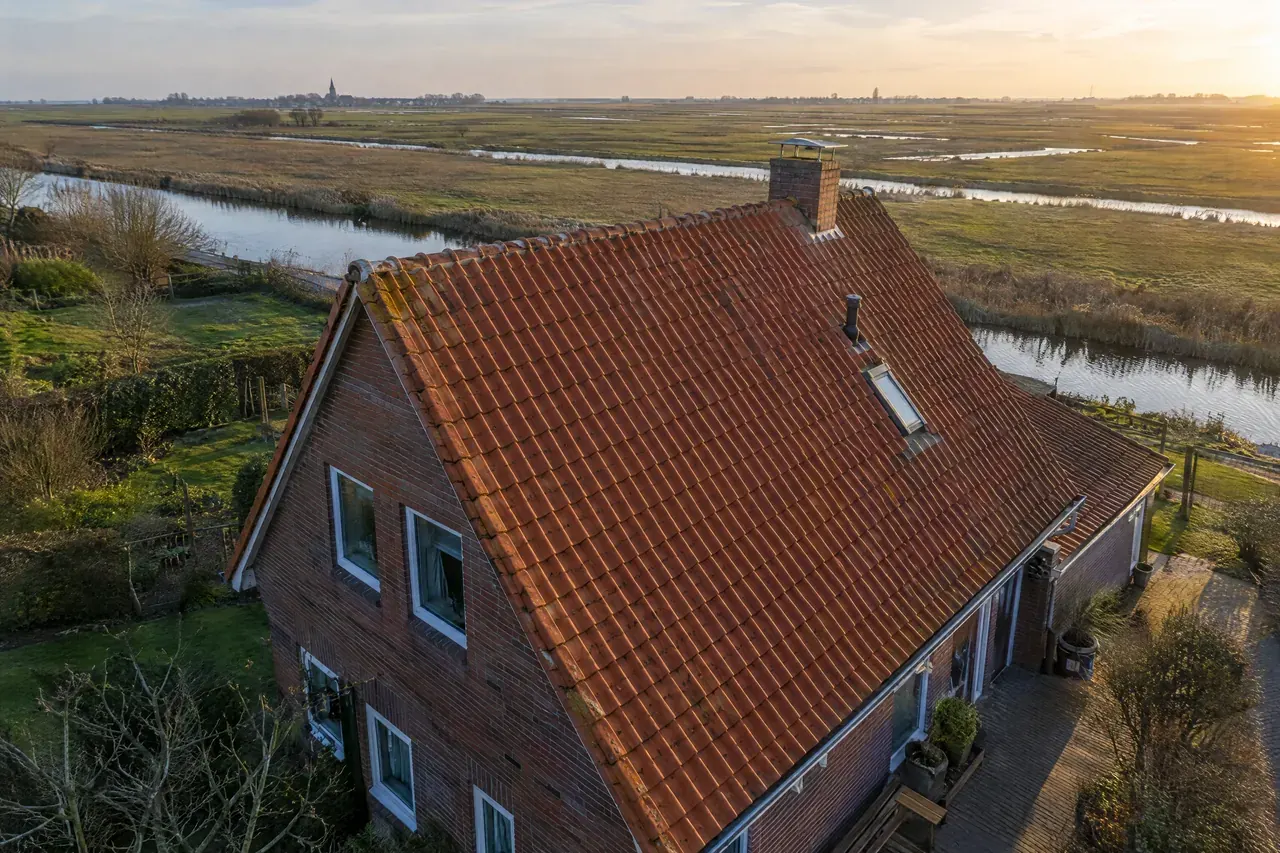 Rotes Tonziegeldach eines Klinkerhauses von oben, dahinter die Marsch im Abendlicht