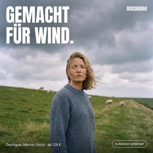 Mode-Anzeige: Frau im blaugrauen Strickpullover auf dem Deich im Wind, Überschrift „Gemacht für Wind.“