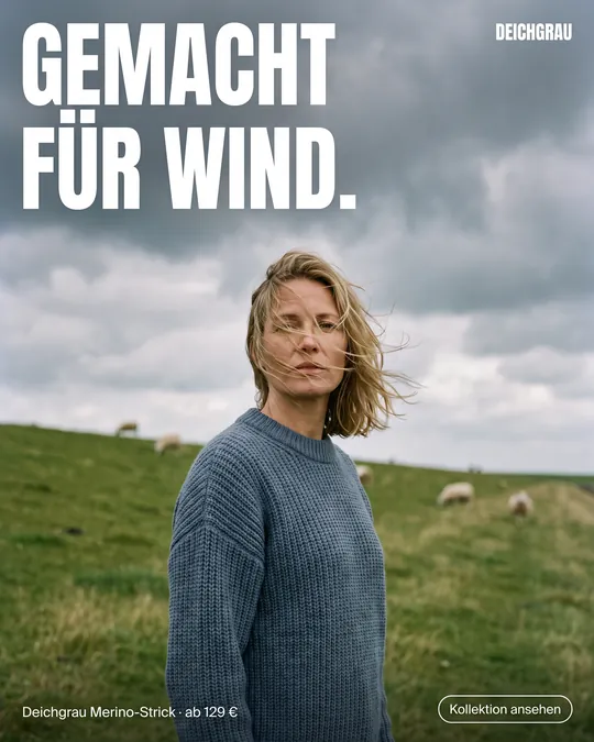 Mode-Anzeige: Frau im blaugrauen Strickpullover auf dem Deich im Wind, Überschrift „Gemacht für Wind.“